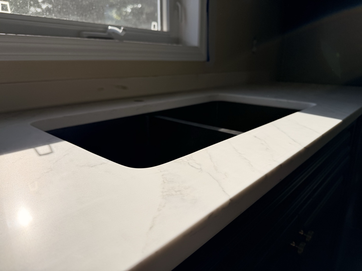 White quartz counter and black undermount sink by a window